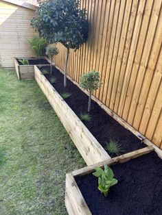 two wooden planters filled with dirt next to a fenced in yard and small trees