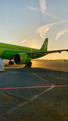 a green airplane sitting on the tarmac at an airport with the sun setting in the background