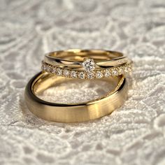 two gold wedding rings with diamond accents on a white lace covered tablecloth in closeup