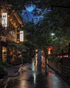 people walking down the street in the rain at night with umbrellas and lights on