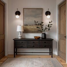 a table with two lamps and a painting on the wall above it in a hallway