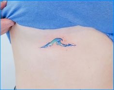 a woman's stomach with a small blue wave tattoo on her side ribcage