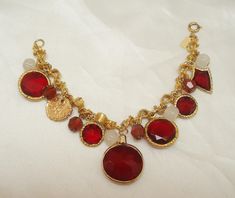 This vintage ruby red glass charm bracelet is truly a standout. The fifteen charm bracelet by Accessocraft is one of their best. The bracelet has faceted glass charms, glass beads, bicolor beads, and a faux Roman coin all attached to a unique goldtone bracelet. There are six faceted red glass charms in goldtone frames. There is a shield, two small rounds, two medium rounds and a large red glass charm. Each glass charm is flat on one side and pointed on the other. In addition there are four white Faberge Jewelry, Brass Cuff Bracelet, Roman Coins, Glass Charms, Red Frame, Copper Pendants, Faceted Glass, White Beads, Red Glass