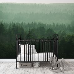 a baby crib in front of a green forest wallpapered with white pillows