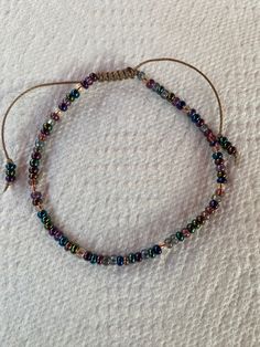 "Rain Ankle Bracelet Bracelet has beautiful 6.0 seed beads tht are blue, purple, green, copper and other  iridescent colors and is made on a Light Brown heavyweight cord that is adjustable.  Simple pull the ends of the strings to adjust for a comfortable fit.    Closes to 7.5\" and opens to approx. 13.5\", if you need to close or open in different size please leave me a note when checking out in Note to Seller Section. If you have any questions you can go to contact seller and I will be happy to help you! Thank you so much for visiting my shop:) Love and Peace,  Lynn" Adjustable Crystal Bracelet With Colorful Beads For Festival, Adjustable Crystal Bracelet With Tiny Beads For Gift, Adjustable Crystal Bracelet With Tiny Beads As Gift, Adjustable Beaded Friendship Bracelets With Heishi Beads, Adjustable Hand-strung Beaded Bracelets For Festivals, Adjustable Beaded Spiritual Friendship Bracelets, Heishi Beads Bracelet With Sliding Knot, Adjustable Spiritual Beaded Friendship Bracelets, Adjustable Beaded Spiritual Friendship Bracelet