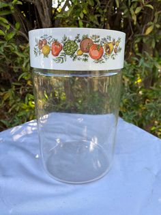 a clear glass with fruits and vegetables painted on the side sitting on a white table cloth