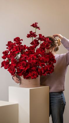 a woman holding a vase with red roses in it and touching the top of her head