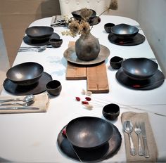 a dining table set with black plates and silver utensils on top of it