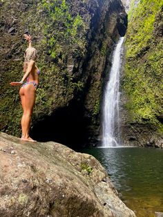 a woman standing on top of a rock next to a waterfall