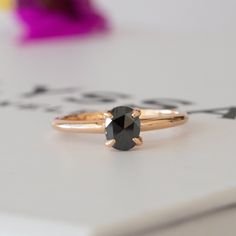 a black diamond ring sitting on top of a white table next to a purple flower