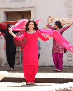 two women in red dresses are holding pink shawls