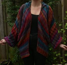 a woman standing in front of a fence with her hands on her hips, wearing a multicolored cardigan