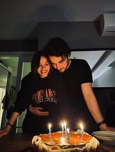 a man and woman standing in front of a cake with lit candles on it that says happy birthday