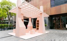 a pink sculpture sitting in front of a building on a brick sidewalk next to trees