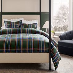 a bed with plaid sheets and pillows in a room next to a couch, chair and window