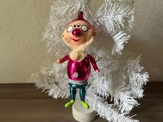 a christmas ornament with a clown face on it's head hanging from a white tree