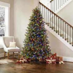 a decorated christmas tree sitting in the middle of a living room next to a stair case