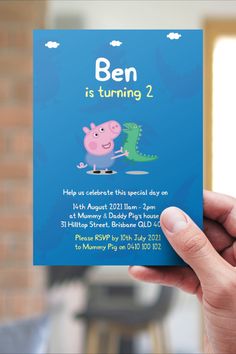 a hand holding up a blue birthday card with pep the pig and dinosaur on it