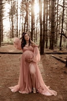 a pregnant woman in a pink dress standing in the woods