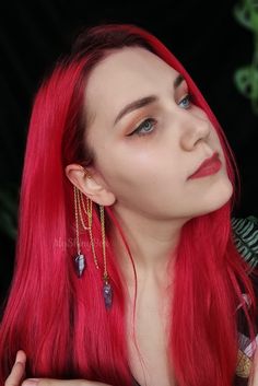 a woman with long red hair and blue eyes wearing gold chains on her necklaces