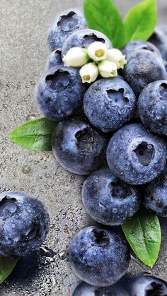 blueberries with green leaves and white flowers on the top one is surrounded by other blueberries