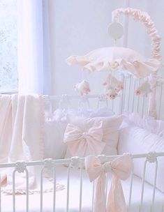 a white crib with pink bows and pillows on it's sides, next to a window