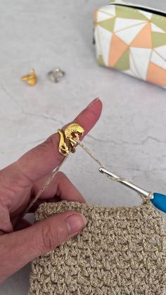 a hand holding a crochet hook in front of a small purse with gold hardware