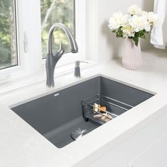 a kitchen sink sitting under a window next to a vase with white flowers in it