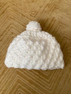 a white crocheted beanie sitting on top of a brown table next to a cell phone