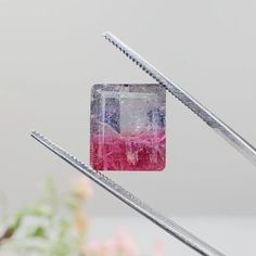 two metal tongs are holding a pink and white square object with holes in it