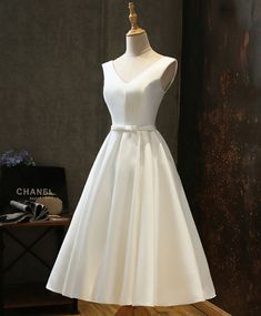 a white dress sitting on top of a wooden floor next to a mannequin