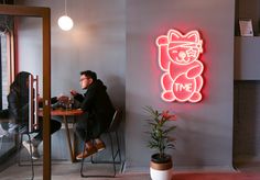 a man sitting at a table in front of a neon sign that says it's time