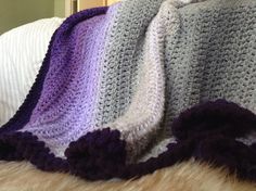 a crocheted blanket on top of a bed next to a white and purple pillow