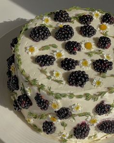 a white cake with blackberries and daisies on it