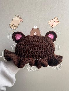 a crocheted brown bear hat with pink ears on it's head is held up in front of a white wall