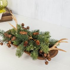 a wooden sleigh filled with pine cones and greenery on top of a white table