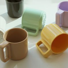 four different colored coffee mugs sitting on a white table next to each other,