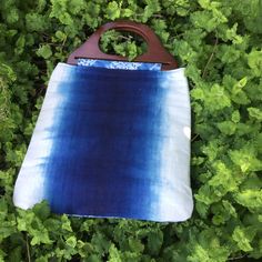 a blue and white bag sitting on top of some green plants with a wooden handle