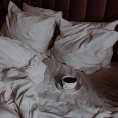 an unmade bed with white sheets and a cup of coffee