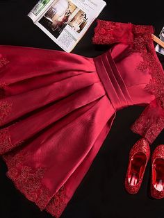 a red dress and shoes on a black surface next to a cell phone, magazine, and other items