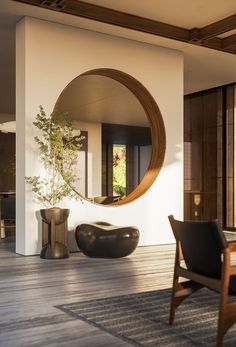 a living room with a large round mirror on the wall and wooden furniture around it