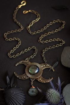 a gold necklace with pearls and other jewelry items on a black surface next to flowers