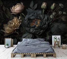 a bed sitting in front of a black wall with flowers on it and two pictures next to it