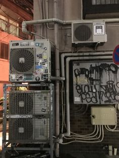 two air conditioners sitting next to each other near a building with graffiti on it