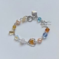 A sweet bracelet. This colorful piece features: ✿ Made with freshwater pearls, glass crystal beads, metal accents, and an assortment of glass beads ✿ Pearlescent peach, iridescent clear, sky blue, neutrals, and silver ✿ Toggle Clasp. Some beads may be added or removed depending on the length selected Kawaii Bracelet, Pastel Bracelet, Bracelet Keychains, Indie Jewelry, Jewelry Accessories Ideas, Freshwater Pearl Bracelet, Clear Sky, Metal Accents, Beaded Accessories