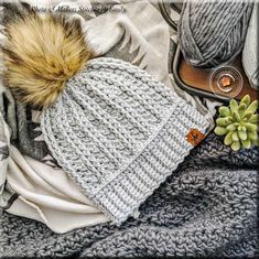 a knitted hat with a fur pom sits on top of a pile of blankets