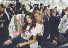 two young women sitting on an airplane and posing for the camera