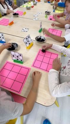 children are sitting at a table with pink and yellow squares on them, playing the game