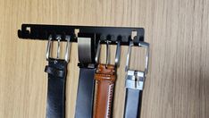 three leather belts hanging on a black metal holder with two different color straps attached to it