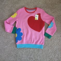 Heavy Pink Sweatshirt Has Multi-Colored Bands, Red Neck, Green Cuffs, And A Blue Banded Waist. The Front Has An Oversized Heavy Red Heart Applique, With Heavy Mod Flower Appliques On Both Sleeves And The Left Side That Wraps Around To The Back. Made Of A Soft Cotton Blend. Size 7/8 Would Look Awesome Paired With Her Favorite Jeans Or Skirt Nwt Never Worn Excellant Condition No Damage Boden Cute Long Sleeve Winter Tops, Cute Long Sleeve Tops For Winter, Playful Crew Neck Sweatshirt For Playwear, Fall Playwear Crew Neck Tops, Crew Neck Tops For Playwear In Fall, Crew Neck Tops For Fall Playwear, Playful Fall Tops For Playwear, Cute Red Long Sleeve Sweater, Playful Cotton Winter Tops